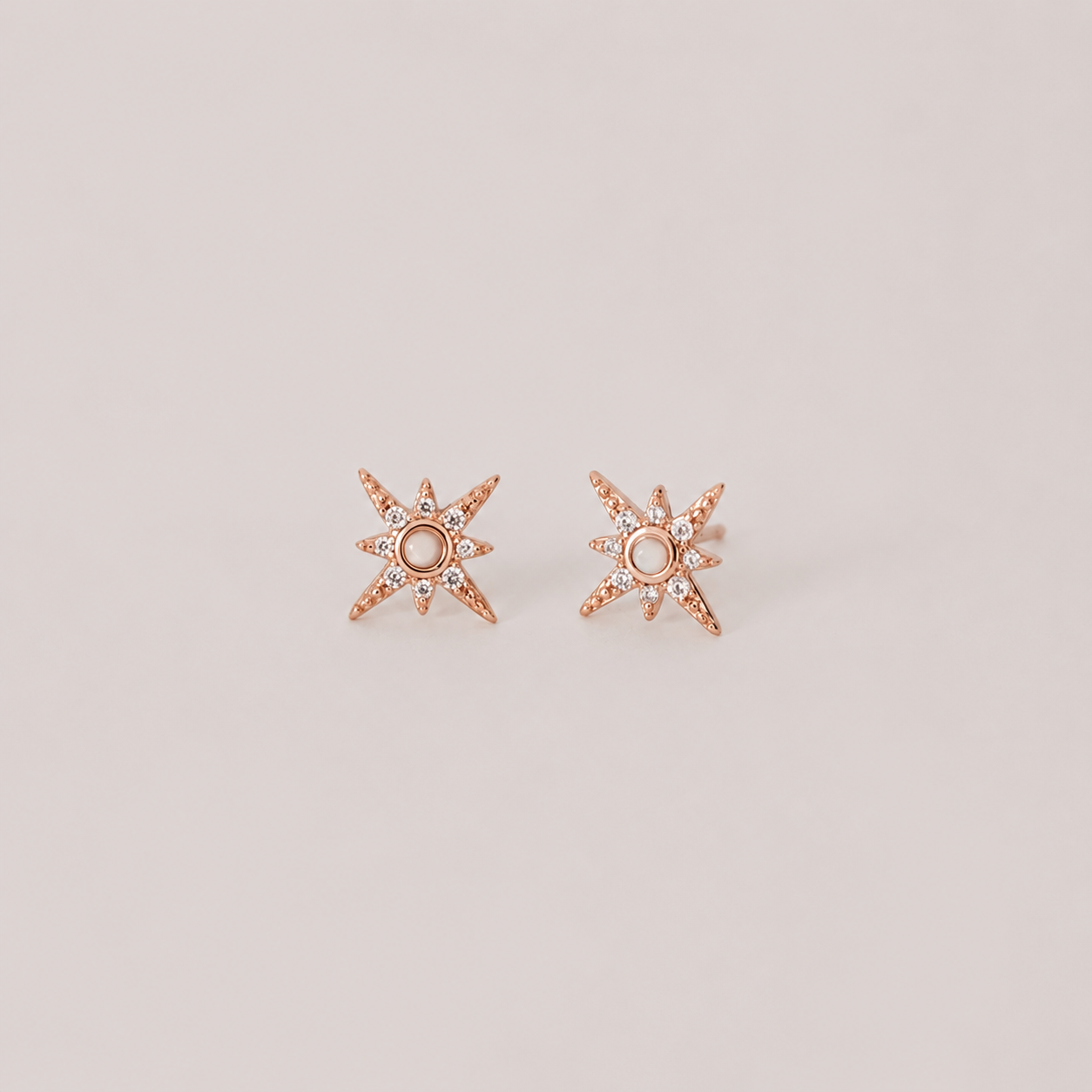 Rose gold star-shaped earrings with small diamonds on a light beige background